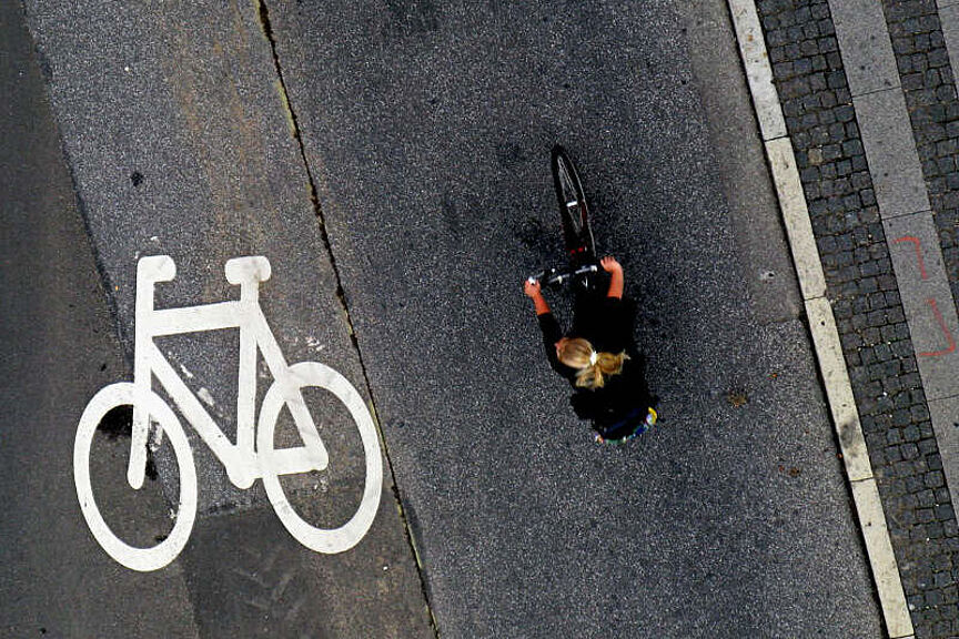 Fahrrad auf der Fahrbahn Von oben fotografiert: Eine Frau fährt mit dem Fahrrad neben einem Fahrradpiktogramm auf der Fahrbahn
