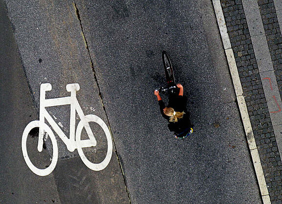 Von oben fotografiert: Eine Frau fährt mit dem Fahrrad neben einem Fahrradpiktogramm auf der Fahrbahn