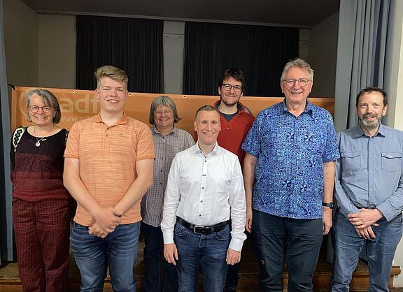 Sieben Personen präsentieren sich lächelnd der Kamera