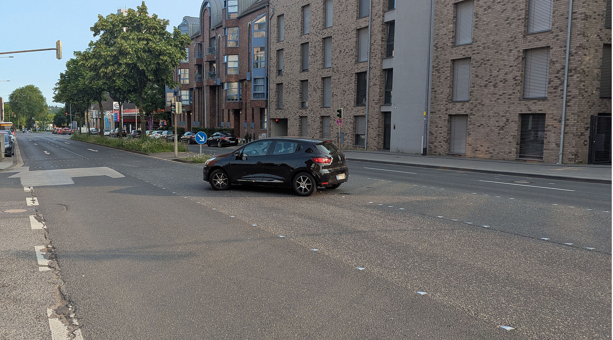 Ein Auto beim linksabbiegen auf der Roermonder Straße. Es sind pro Fahrtrichtung zwei Fahrspuren zu sehen. Daneben sind in beide Richtungen Parkbuchten angelegt. Der Gehweg wirkt am Straßenrand gerade zu verloren