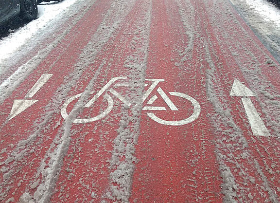 Fahrradpiktogramm auf rot gefärbtem Asphalt mit Schneematsch