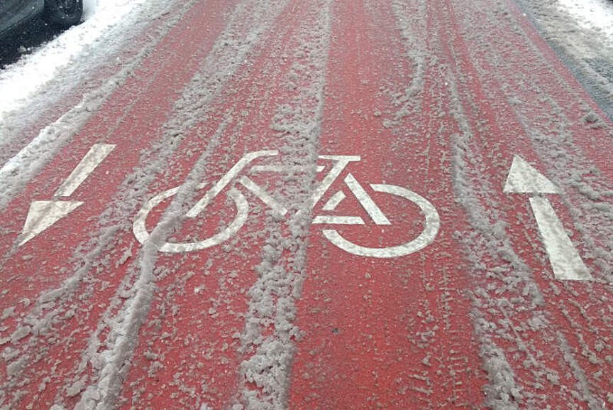 Fahrradstraße im Schnee Fahrradpiktogramm auf rot gefärbtem Asphalt mit Schneematsch