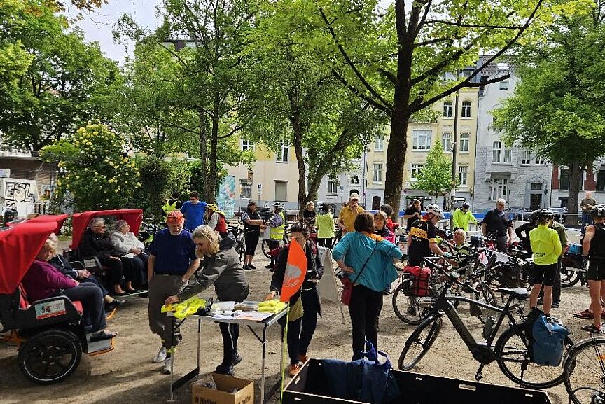 Newsletter 2025-02 Das Foto zeigt einen Infostand mit vielen Radfahrenden im Schatten unter Bäumen