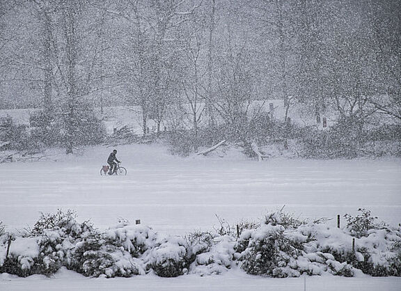 Jemand fährt im Schneegestöber mit dem Fahrrad über einen zugefrorenen See