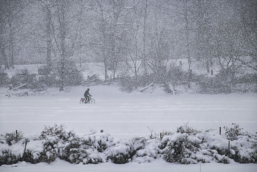 Mit dem Fahrrad auf zugefrorenem See Jemand fährt im Schneegestöber mit dem Fahrrad über einen zugefrorenen See