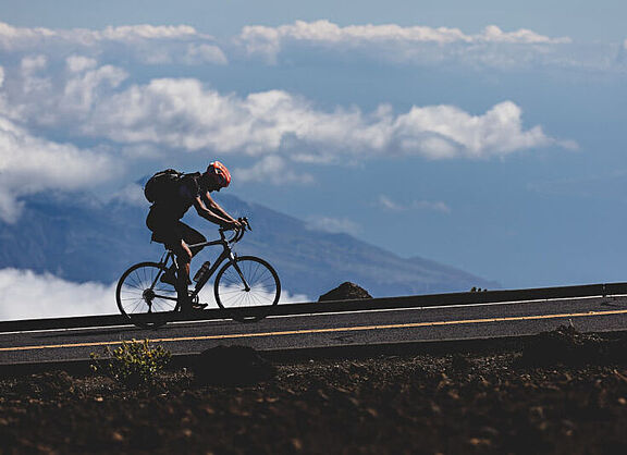 Ein Radfahrer im Gebirge; im Hintergrund sind unter ihm Wolken zu sehen