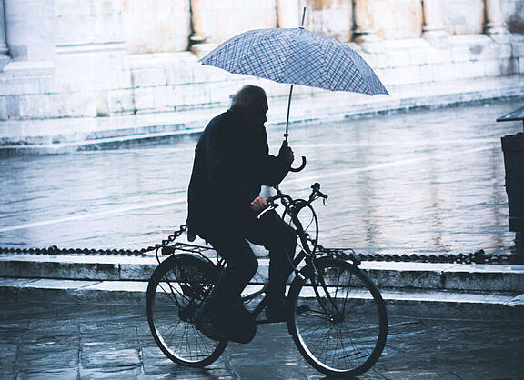 Ein Mann hält während des Fahrradfahrens einen Regenschirm in der Hand