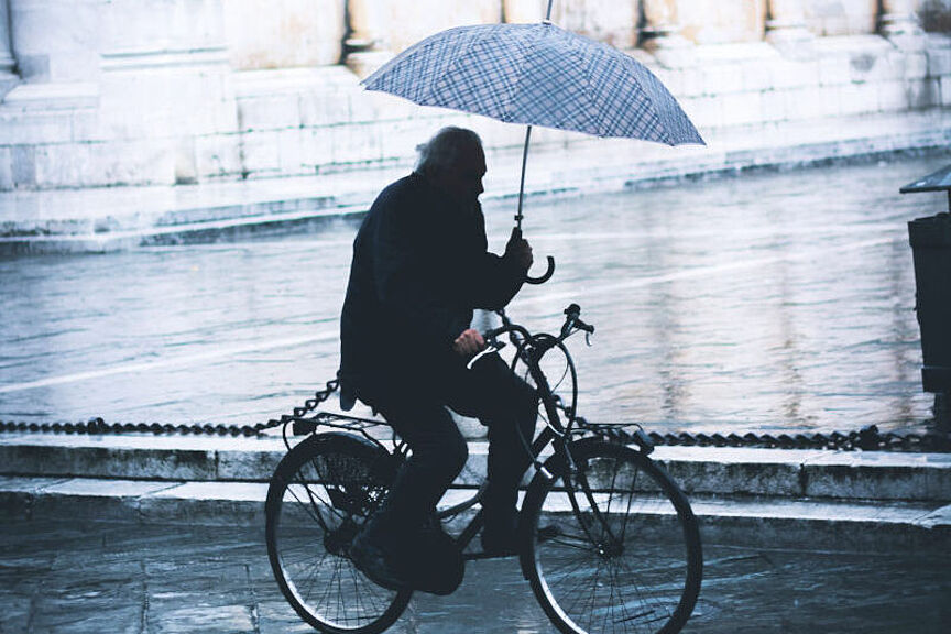 Radfahren im Regen Ein Mann hält während des Fahrradfahrens einen Regenschirm in der Hand