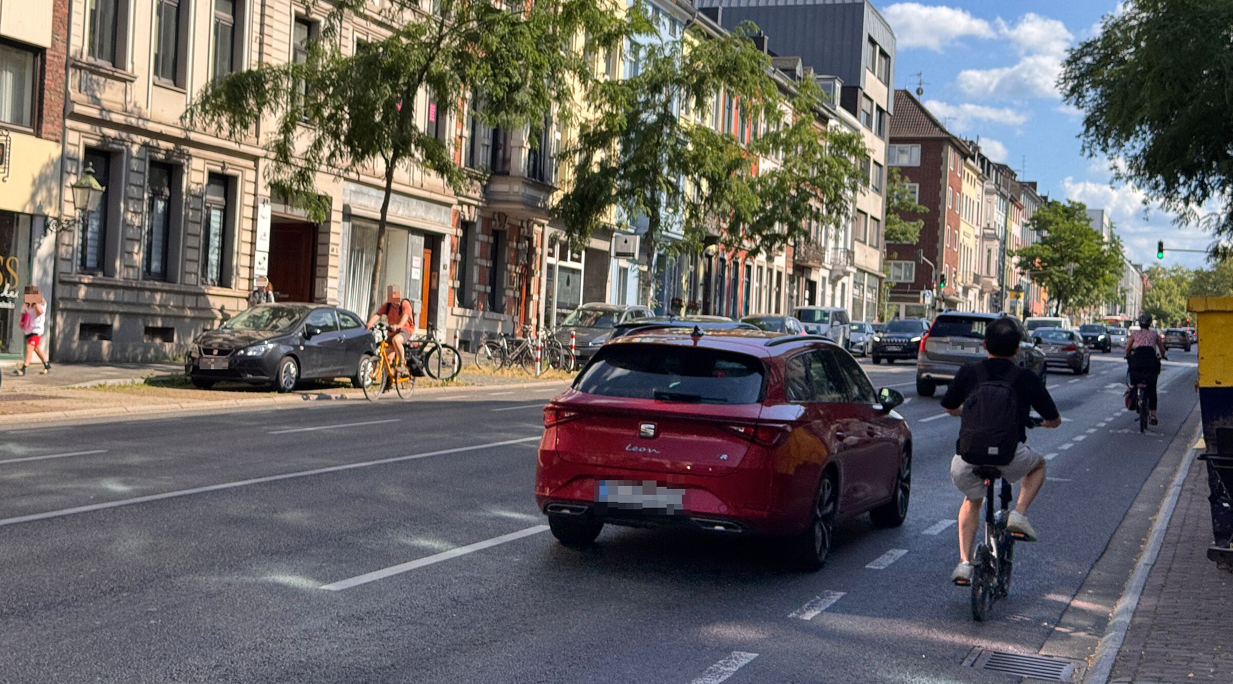 Zwei Radfahrende fahren auf der Wilhelmstraße neben Autos und einem Lieferfahrzeug. Die Radverkehrsführung ist schmal markiert und liegt unmittelbar neben dem Kfz-Verkehr.