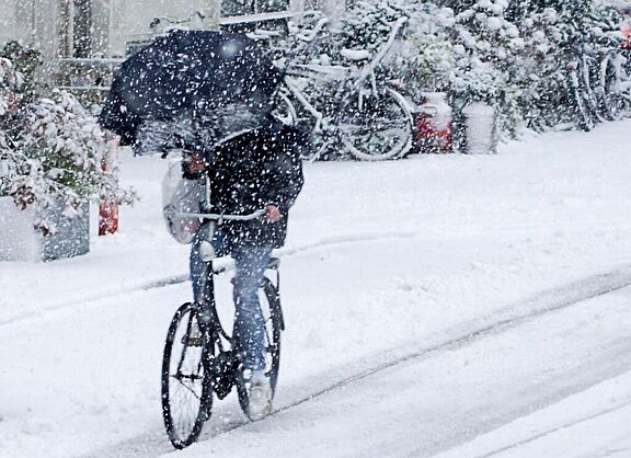 Ein Mann fährt mit dem Fahrrad durch dichtes Schneetreiben und hält einen Regenschirm in der Hand