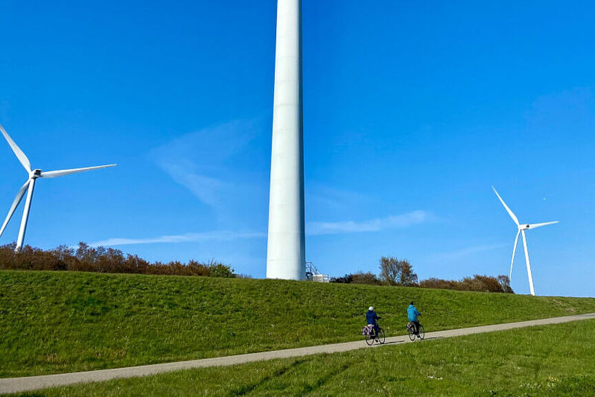 Wind- und Fahrräder Zwei Personen fahren auf einem Weg vor drei Windräder Fahrrad