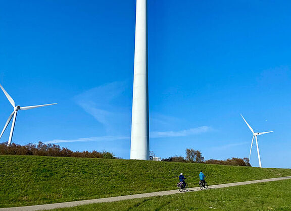 Zwei Personen fahren auf einem Weg vor drei Windräder Fahrrad