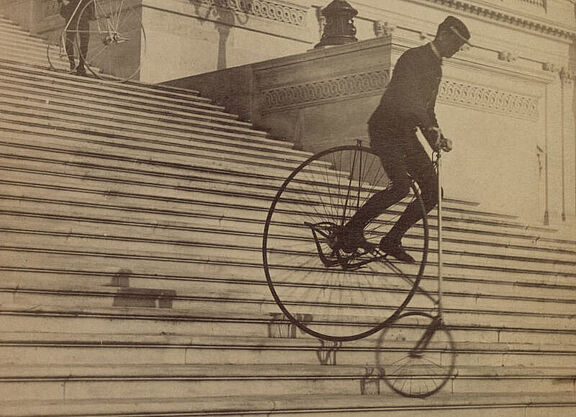 Historisches Foto: Ein Mann fährt mit einem Hochrad eine große Treppe hinunter