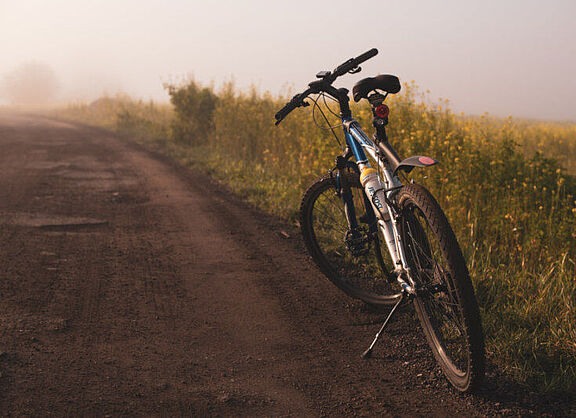 Auf einem Feldweg abgestelltes Fahrrad, im Hintergrund Felder im Nebel