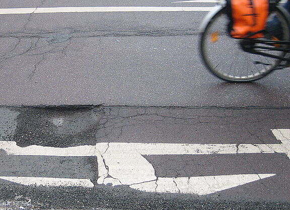 Ein Schlagloch auf der Straße, man sieht noch das Hinterrad eines vorbeifahrenden Fahrrads.