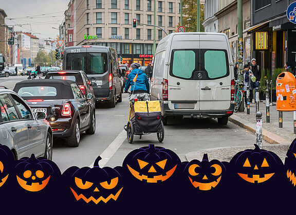 Die Straßenszene in Berlin zeigt einen Radfahrer mit gelbem Anhänger, der sich zwischen Autoss seinen Weg bahnt.